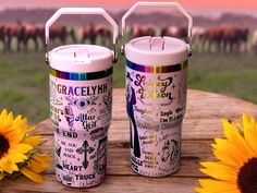 two travel mugs sitting on top of a wooden table next to sunflowers