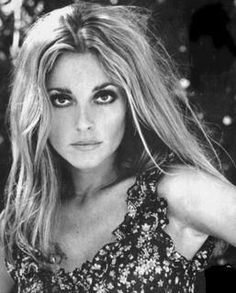 a black and white photo of a woman with long hair wearing a floral top, posing for the camera