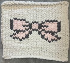 a crocheted dishcloth with black and pink designs on it, sitting on a tile floor