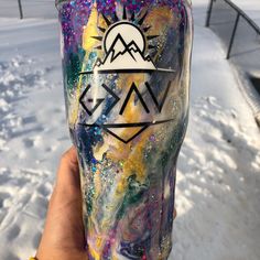 a hand holding up a painted cup in the snow