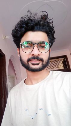 a man with black hair wearing glasses and a white t - shirt is looking at the camera