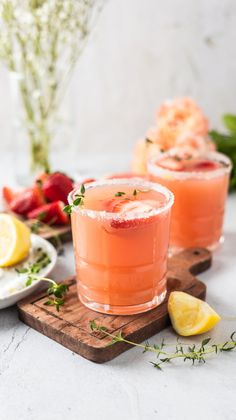 two glasses filled with pink lemonade and garnished with fresh herbs on a cutting board