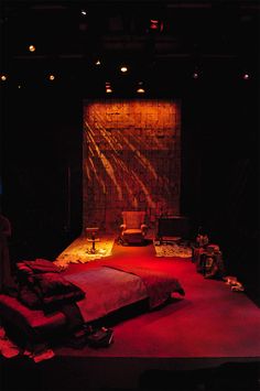 an empty stage with a bed and red lights on it's sides, in front of a brick wall