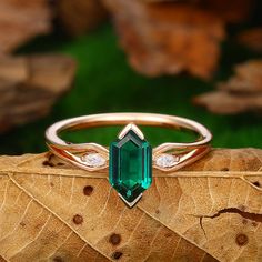 an emerald colored ring with two diamonds on top of it, sitting on a leaf