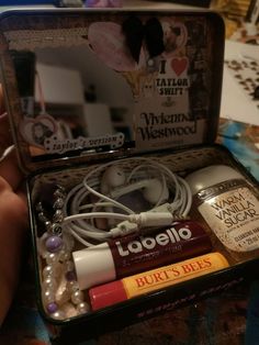 an open tin box containing various items including earbuds, nail polish and lipstick