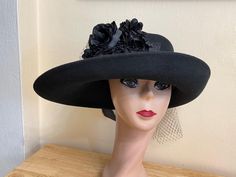 This unique shape black wide-brimmed wool felt hat would be perfect for any special occasion. The measurements are 16 inches by 12 inches. The hat is trimmed with a black raw edged silk ribbon band, assorted black silk and satin flowers, one large silk rose , velvet leaves and removable netting all around the band. The hat will fit up to a 22 5/8 inch head size and has a sizing cord inside to adjust to your head size. NOTE: Please check the head size before purchase, I am happy to answer any questions you may have. There will be a 30% restocking fee for this hat if returned. Formal Black Wool Felt Hat, Black Wool Felt Hat For Formal Occasions, Formal Black Wide Brim Costume Hat, Black Curved Brim Costume Hat For Church, Formal Black Wool Hat, Black Costume Hat With Curved Brim For Church, Black Costume Hat For Church With Curved Brim, Black Costume Hats For Church, Black Wool Top Hat With Curved Brim