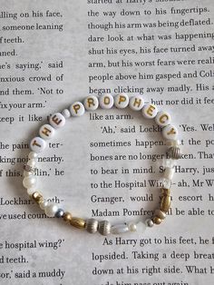 a white bracelet with gold letters and pearls on top of an open page of a book