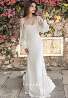 a woman standing in front of flowers wearing a white dress with sheer shoulders and long sleeves