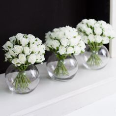 three clear vases filled with white flowers on top of a counter next to a mirror