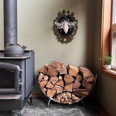 a pile of firewood sitting next to a stove in a room with a clock on the wall