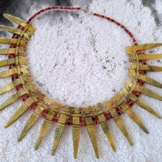 a gold necklace with red beads and spikes on it's collarline, sitting on a white surface