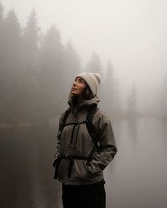 a person standing in front of a body of water on a foggy day with trees