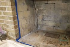 an unfinished shower with blue tape on the wall and floor in front of it, next to a brick wall