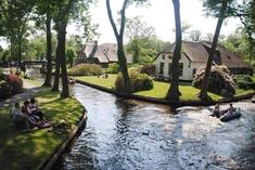 people are sitting on the bank of a river in front of some houses and trees