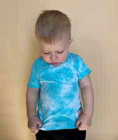 a little boy standing in front of a wall with his hands on his hips and looking down