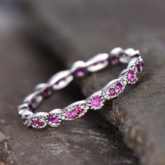 a wedding band with pink sapphires and white diamonds on top of a rocky surface