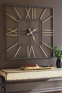 a large metal clock mounted to the side of a wall next to a table with a plant