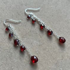 two pairs of red glass beads hanging from silver earwires on a stone surface