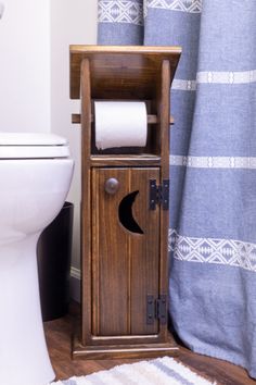 a wooden cabinet sitting next to a toilet in a bathroom under a blue shower curtain