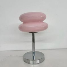 a pink table lamp sitting on top of a metal stand next to a white wall