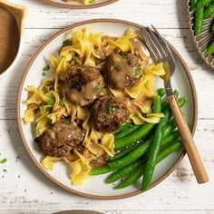 two plates filled with pasta and meatballs next to green beans on a white table