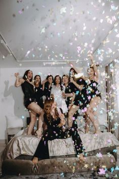 a group of women standing on top of a bed with confetti falling around them