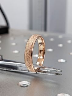 two gold wedding bands sitting on top of a metal table with rivets around them