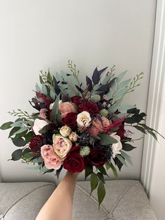 a woman's hand holding a bouquet of red and pink flowers in front of a white wall