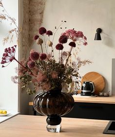 a vase filled with lots of flowers sitting on top of a wooden table next to a wall