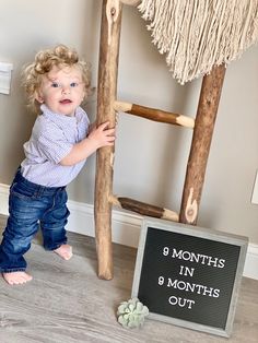 a toddler standing next to a wooden ladder and sign that says 9 months in 6 months out