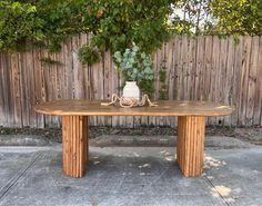 a wooden table sitting in front of a fence with a vase on top of it