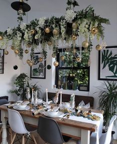 a dining room table set for christmas dinner with white and gold decorations hanging from the ceiling