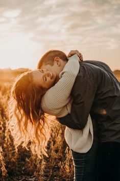 a man and woman are hugging in the middle of a field at sunset with their heads touching each other