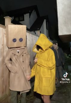 two people in yellow coats holding hands and standing next to each other with cardboard boxes on their heads