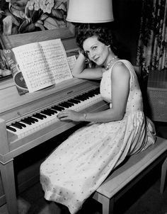 a woman sitting at a piano in front of a painting