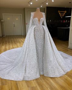 a white wedding gown on display in a room with wood flooring and lights hanging from the ceiling