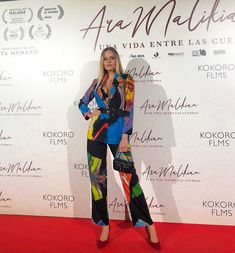 a woman standing on top of a red carpet next to a white wall wearing colorful clothing