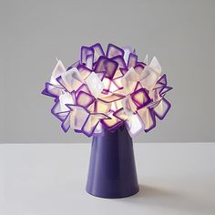 a purple vase filled with lots of white and purple glass flowers on top of a table