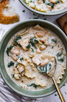 two bowls filled with pasta and spinach covered in white sauce on top of a table