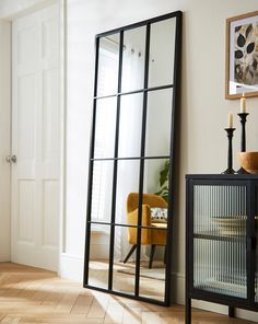 a mirror sitting on top of a wooden floor next to a cabinet with candles in it