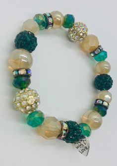 "The highlight of this handmade beaded stretch bracelet is the emerald and gold sparkle ball beads. These colourful crystallized beads complement the iridescent crystal spacer beads in antique gold throughout the bracelet. The rest of the bracelet is made up of green and gold beads in a variety of shapes, sizes and iridescent sheens. As the bracelet moves with wear the beads catch the light, emphasizing the unique sparkle and shimmer of the piece.  Each piece of jewelry from my store features the signature \"made with love\" heart charm. Includes a white organza bag to store." Green Stretch Bracelet With Faceted Round Beads, Green Spiritual Beaded Bracelets With Faceted Beads, Spiritual Green Beaded Bracelets With Faceted Beads, Green Crystal Round Bracelets, Green Beaded Bracelet With Gold Beads, Green Crystal Bracelet With Colorful Beads, Green Crystal Round Beads Bracelets, Crystal Stretch Bracelet With Faceted Beads, Green Crystal Beaded Bracelets With Round Beads