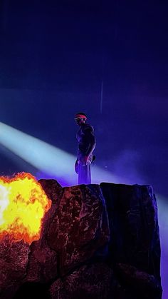 a man standing on top of a large rock next to a bright yellow fireball