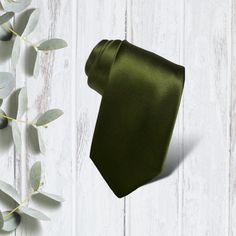 a green tie sitting on top of a white wooden floor next to eucalyptus leaves and an olive branch