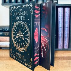 the crimson moth book is open on a table next to bookshelves and a clock