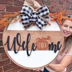 a woman holding up a welcome sign in front of a brick wall with pumpkins