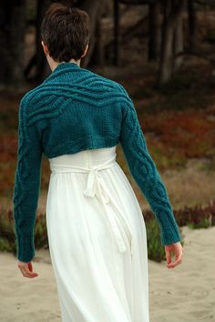 a woman is walking on the beach in a white dress and green cardigan sweater