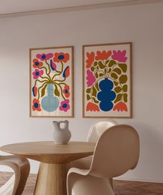 two paintings on the wall above a round table with white chairs and a vase in front of it