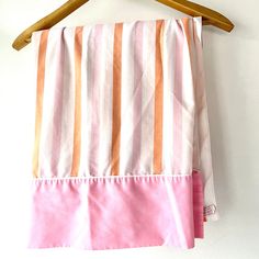 a pink and orange striped towel hanging on a wooden hanger next to a white wall