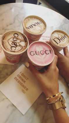 three cups of coffee with the word gucci written on them are being held by two hands