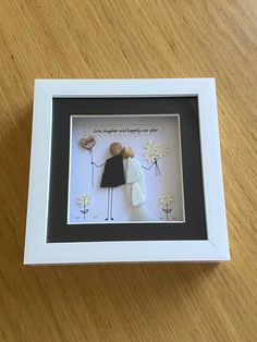 a white frame with a couple holding hands and flowers in the center on a wooden table